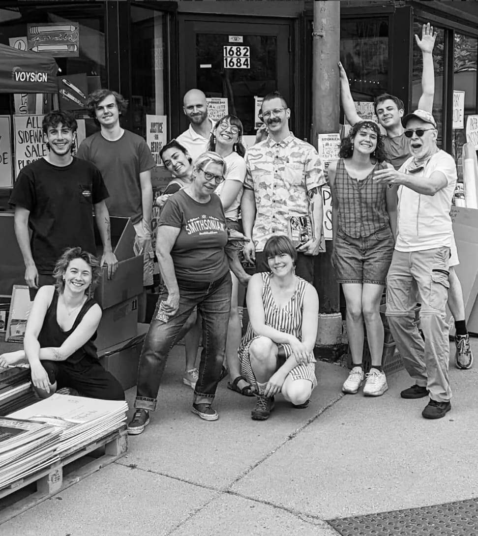 Group of smiling employees posing outside of their store.
